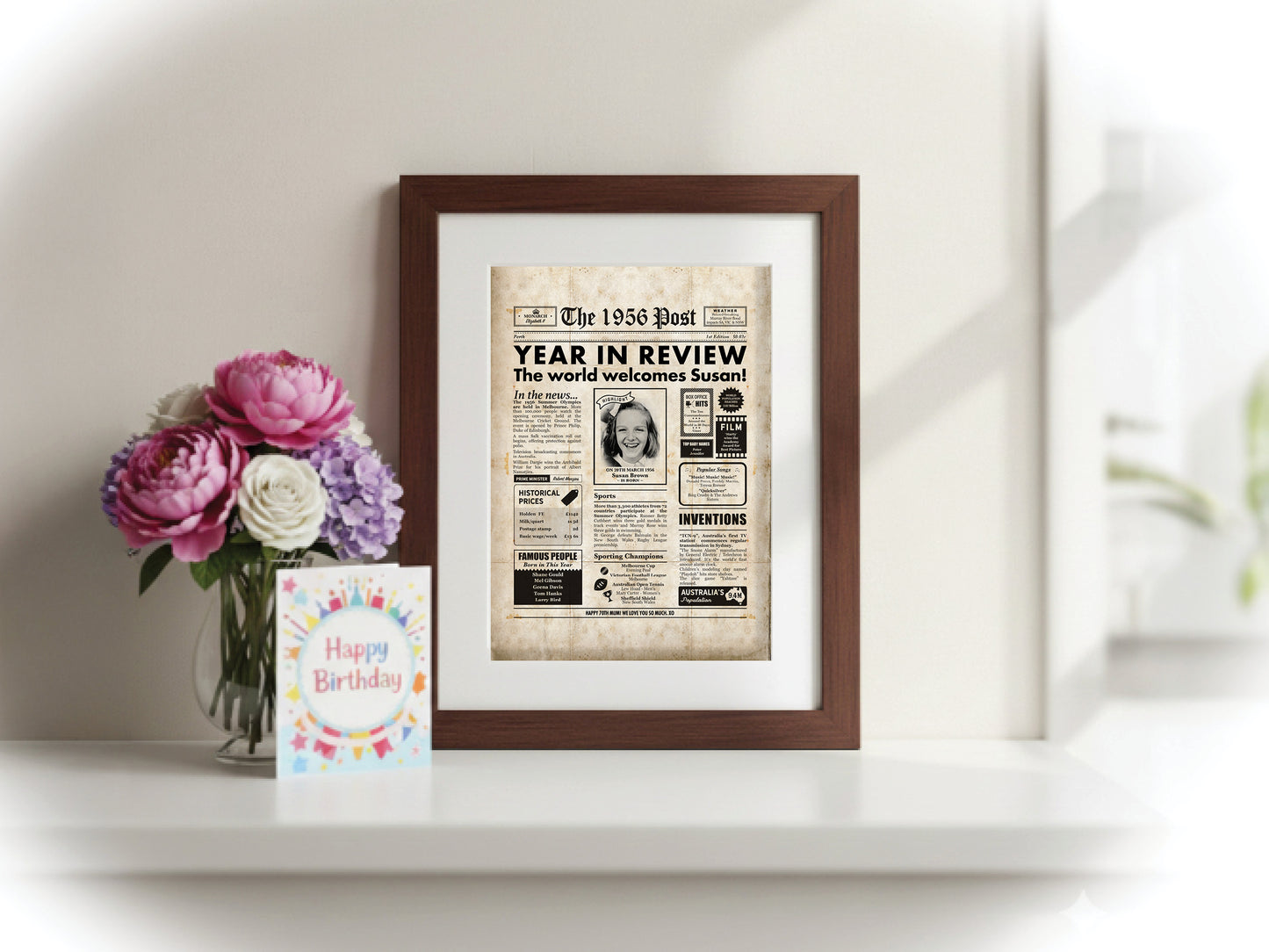 70th birthday digital newspaper poster print, featuring aged paper textures, framed, beside flowers and a birthday card.